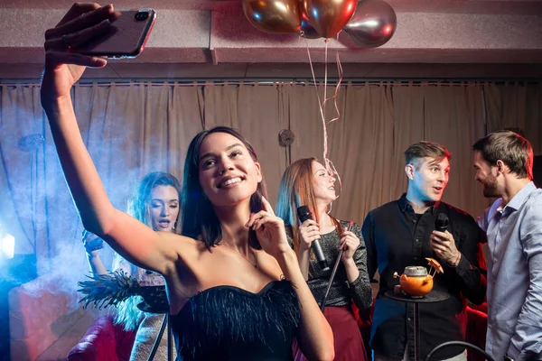 Çekici bir kadın arkadaşlarıyla karaoke yaparken fotoğraf çekiyor. — Stok fotoğraf