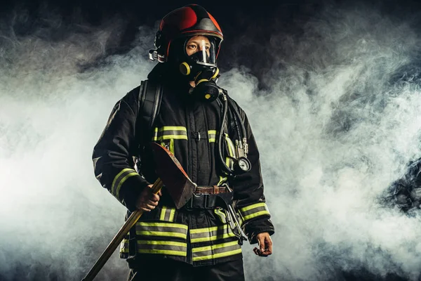 Bombeiro caucasiano com martelo arriscando sua vida para salvar as pessoas do fogo — Fotografia de Stock
