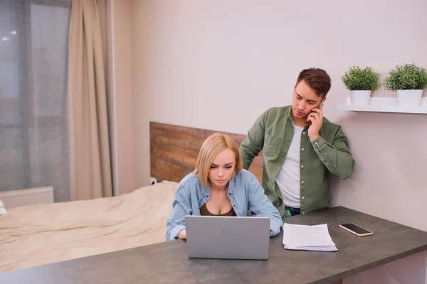 女人在笔记本电脑上工作，而丈夫在电话里说话 — 图库照片