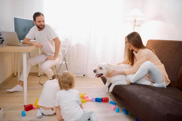 Děti si spolu hrají na podlaze, zatímco mladí rodiče relaxují doma — Stock fotografie