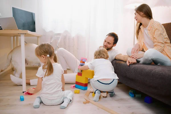Kinderen spelen samen op de vloer terwijl jonge ouders ontspannen thuis — Stockfoto