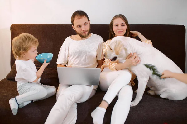 Familia caucásica feliz descansando en casa con el perro y el ordenador portátil —  Fotos de Stock