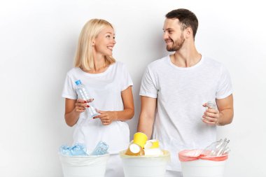 Ellerinde cam ve plastik şişelerle birbirlerine bakan hoş bir adam ve kadın.