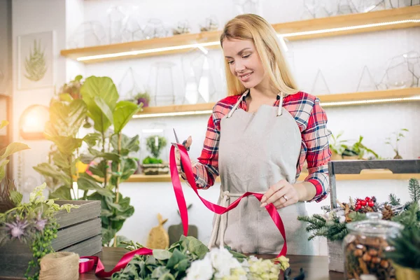 Hermosa feliz joven florista hembra de pie en invernadero lleno de flores — Foto de Stock