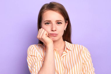 Cute female student keeps hand under chin, feels tired and bored at lesson