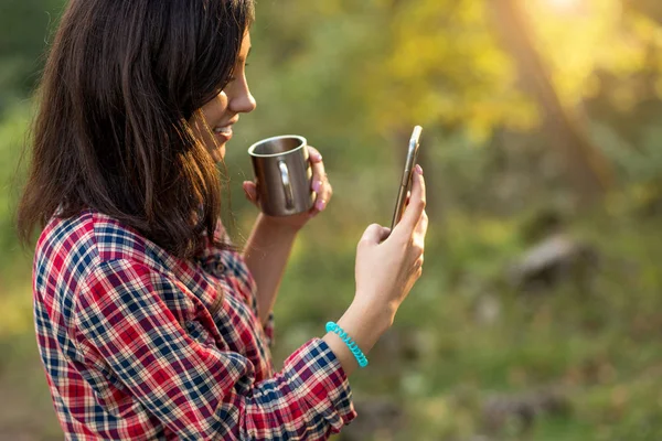 Веселая молодая женщина с помощью смартфона, пьет чай . — стоковое фото