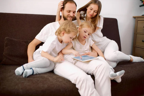 Família amigável em roupas casuais sentar no sofá em casa usando tablet — Fotografia de Stock