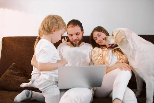 Família caucasiana feliz descansando em casa com cão e laptop — Fotografia de Stock