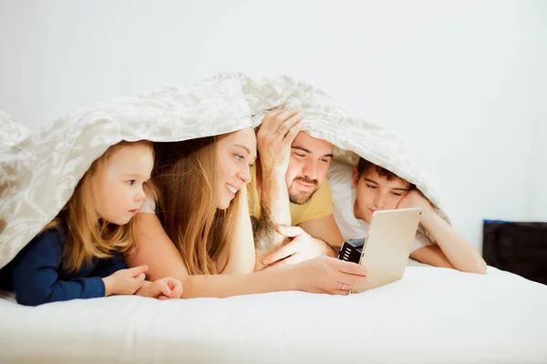 Bela família deitada sob cobertor e assistir a vídeos em tablet — Fotografia de Stock