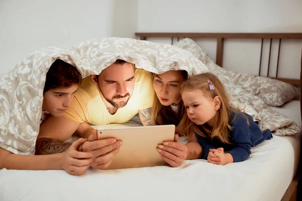 Vriendelijke Kaukasische familie onder deken op bed kijken video 's — Stockfoto
