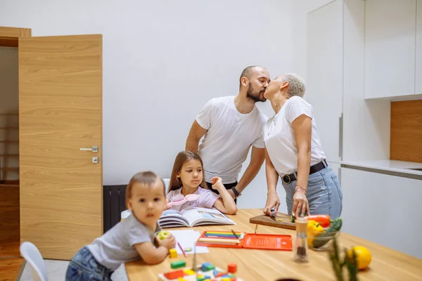 Family couple kissing while their children sitting under them at table — Stock Photo, Image