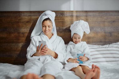 Kızı olan çekici bir kadın cep telefonuyla yatağa uzanıyor.