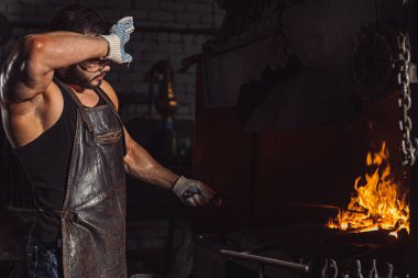 Yorgun demirci atölyede metal ısıtıyor.