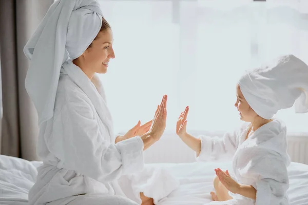 little girl playing clapping game with mom sitting on bed together