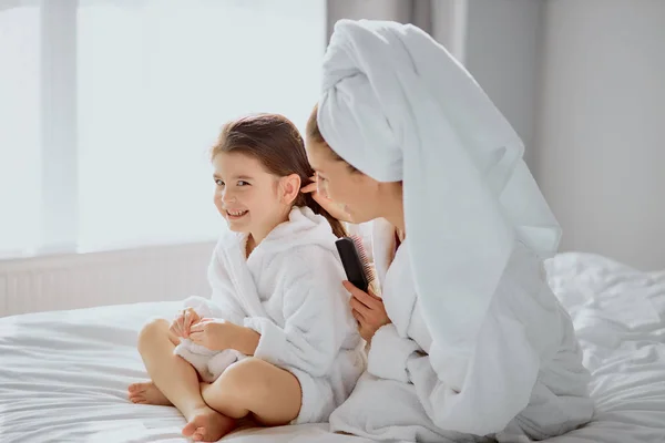 Alegre familia amistosa de madre e hija peinando el pelo en la cama —  Fotos de Stock
