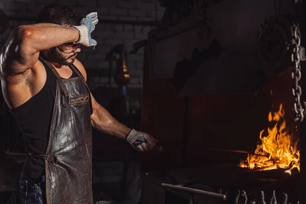 Втомлений коваль чоловік нагріває метал в майстерні — стокове фото