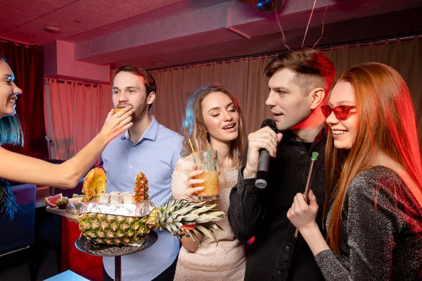 Group of young people singing into microphone in karaoke bar — Stock Photo, Image