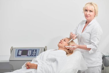 blonde talented cosmetologist performing microcurrent procedure at beauty salon clipart