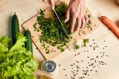 Kadın elleri vejetaryen salatası yapıyor, ahşap tahtada soğan kesiyor.