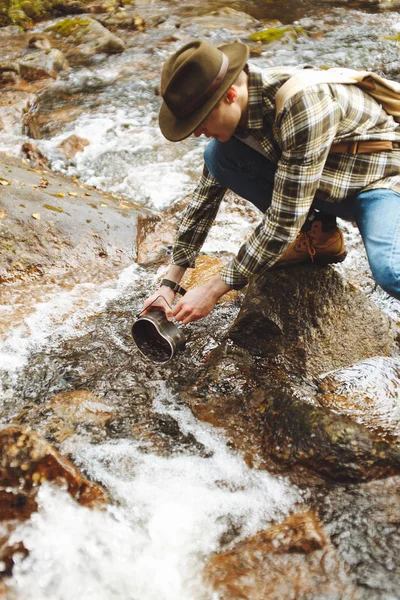 Mladý muž v kostkované košili. džíny přinášející vodu z potoka — Stock fotografie