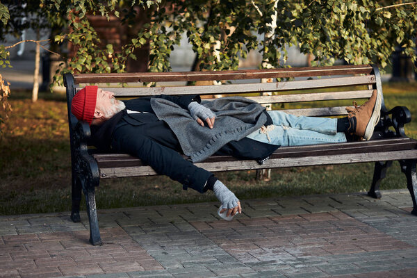 Vagabond male sleeping on bench during the day