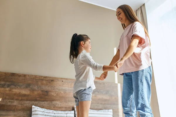 Happy woman jumping on bed with daughter — Stock Photo, Image
