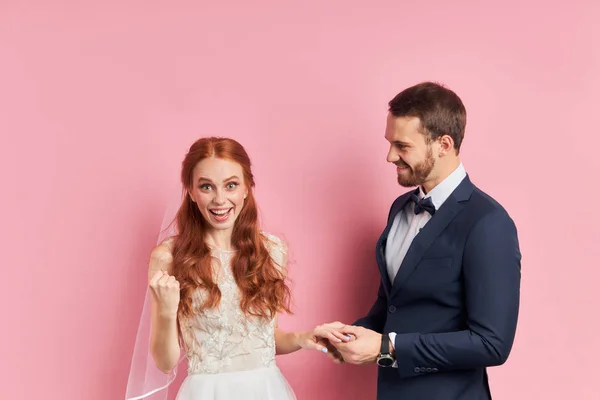 Mulher bonita alegre e homem vestindo smoking e vestido de casamento branco isolado sobre ackground rosa — Fotografia de Stock