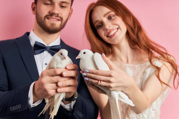 Sorrindo homem e mulher segurando pombos em mãos isoladas sobre fundo rosa — Fotografia de Stock