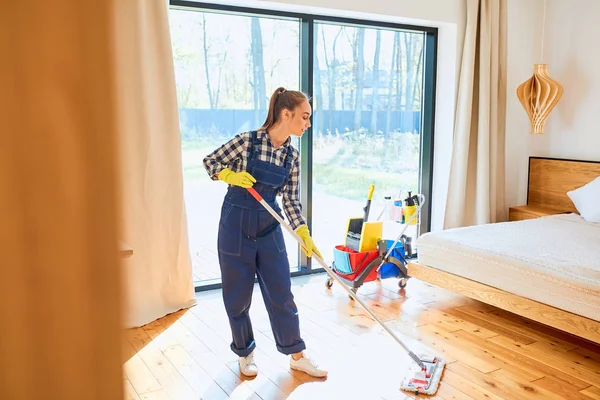 Doncella en uniforme azul limpiando piso en dormitorio —  Fotos de Stock