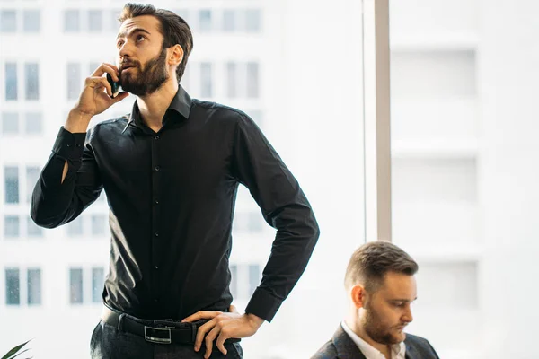 Szakállas elfoglalt férfi beszélgetés telefonon az irodában — Stock Fotó