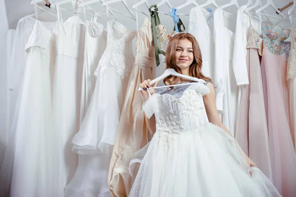 Jovem sorridente noiva olhar para vestido de noiva bonita — Fotografia de Stock