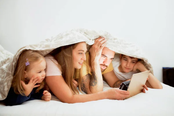 Amigable caucásico familia bajo manta en cama viendo vídeos —  Fotos de Stock