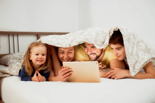 Vriendelijke Kaukasische familie onder deken op bed kijken video 's — Stockfoto