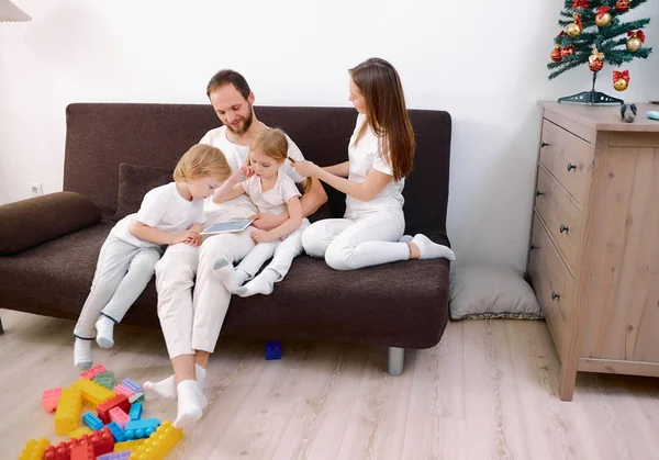 Приваблива щаслива сім'я складалася з матері, батька, сина і дочки, що сидить на дивані вдома з планшетом — стокове фото