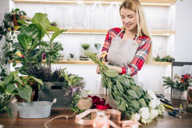 Çiçeklerle dolu serada duran güzel, mutlu, genç bir çiçekçi kadın.