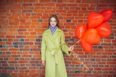 Kırmızı balonlu, ceketli, gülümseyen bir kadın.