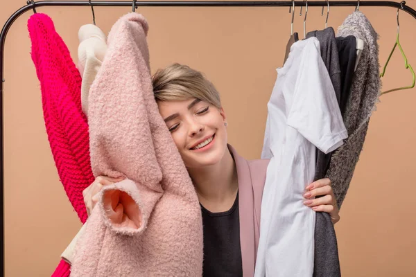 Agradable chica está abrazando toda la ropa en la tienda como ella quiere comprar todos ellos —  Fotos de Stock