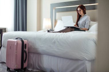 Otel odasında dizüstü bilgisayar ile yatakta yalan zarif kadın giyinmiş.