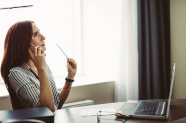 Masada oturan ve dizüstü bilgisayarda çalışan Kızıl saçlı kadın