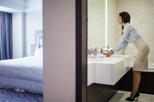 Όμορφη γυναίκα σε επίσημη ένδυση κοιτάζοντας καθρέφτη ενώ πλένετε τα χέρια στο μπάνιο — Φωτογραφία Αρχείου