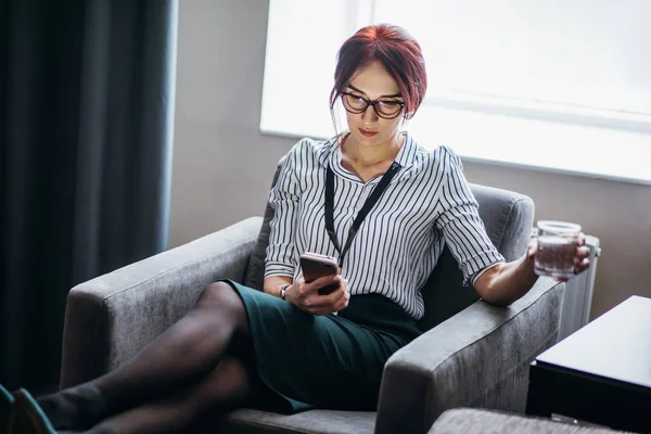 Femme d'affaires est assis dans un fauteuil avec verre d'eau à la main et parler au téléphone — Photo