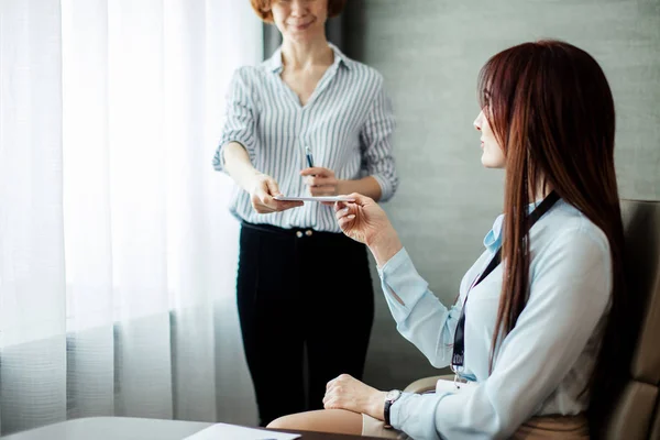 Vänlig kvinnlig chef ger en lapp till sin assistent flicka diskuterar uppgifter på kontoret. — Stockfoto