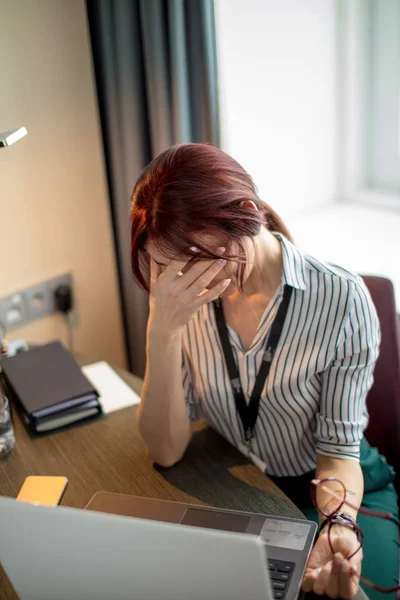 Young red-haired woman sitting at table and working on laptop — Stock Photo, Image