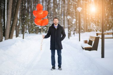 young handsome guy in coat with red air balloons