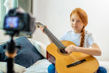 Küçük beyaz kız kameraya gitar çalıyor.