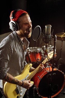 Genç muhteşem müzisyen elektro gitar çalıyor ve stüdyoda şarkı söylüyor.