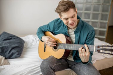 Genç beyaz adam evde akustik gitar çalıyor.