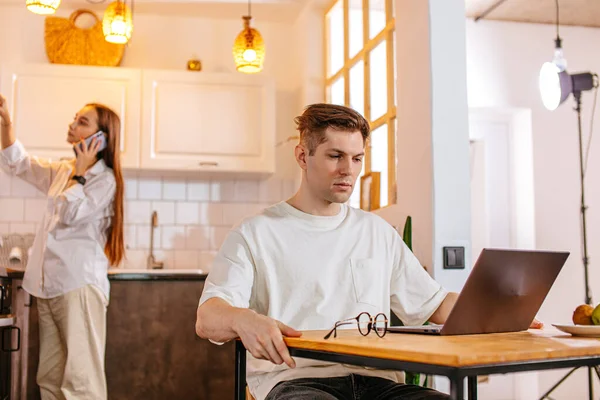 Attraktive Frau telefoniert, während ihr Mann am Laptop arbeitet — Stockfoto