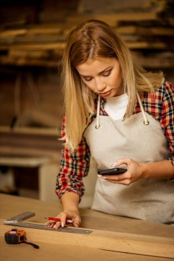 Genç marangoz kadın cep telefonu kullanıyor.