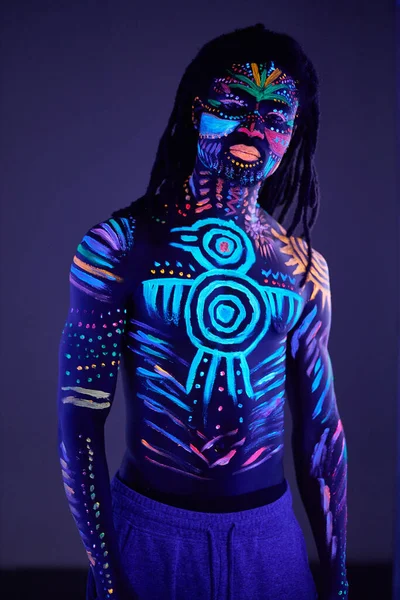 Hombre africano pintado en pintura fluorescente en la cara y el torso muscular —  Fotos de Stock
